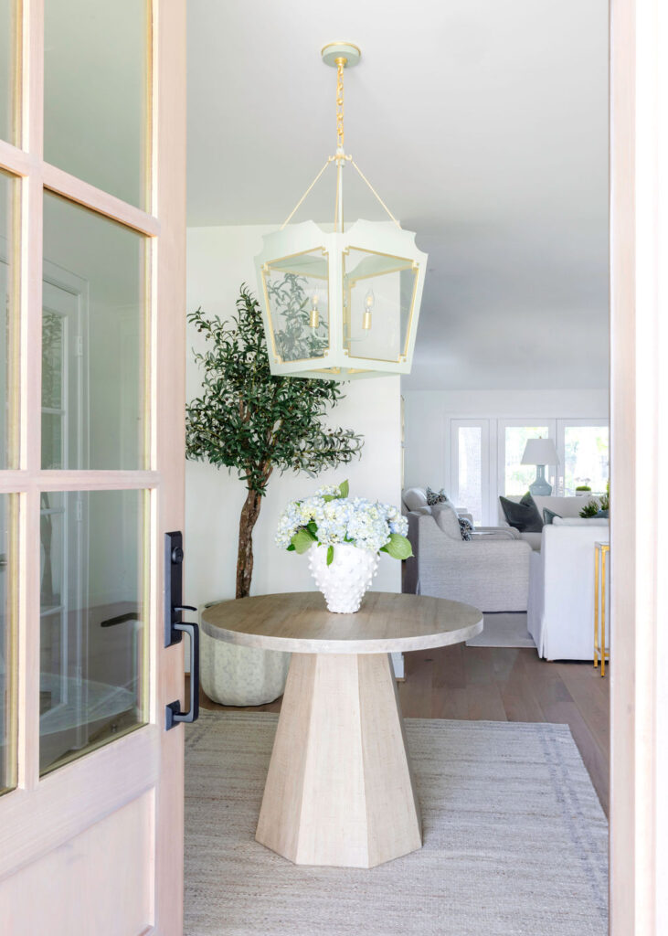 Step into the revamped foyer and wow! You can't miss that bold, classic pendant light flaunting a super fun color. It's hanging right above a chic, round entry table that screams "welcome." Adding some serious style points, there's a stunning faux olive tree bringing in those natural tones, perfectly matched with a cool, earthy rug.