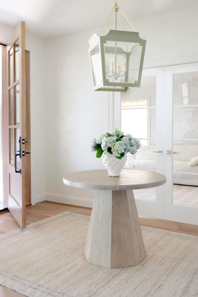 Step into the revamped foyer and wow! You can't miss that bold, classic pendant light flaunting a super fun color. It's hanging right above a chic, round entry table that screams "welcome." Adding some serious style points, there's a stunning faux olive tree bringing in those natural tones, perfectly matched with a cool, earthy rug.