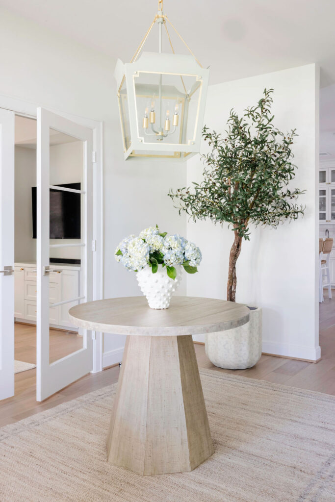 Step into the revamped foyer and wow! You can't miss that bold, classic pendant light flaunting a super fun color. It's hanging right above a chic, round entry table that screams "welcome." Adding some serious style points, there's a stunning faux olive tree bringing in those natural tones, perfectly matched with a cool, earthy rug.